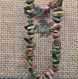 A multicolored Unakite bracelet with varying shades of green and red, showcased on a woven beige background.