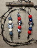Three beaded freshie hangers / lanyards with cow and skull designs on a textured fabric background