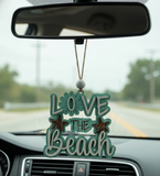 Car charm with 'Love the Beach' text hanging from a car's rearview mirror.