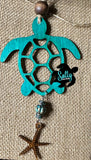 A wooden car charm in the shape of a sea turtle with a turquoise patterned shell, hanging from a string.