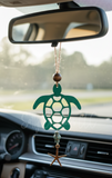 Green turtle-shaped car air freshener hanging from a car's rearview mirror.