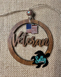 A wooden car charm with the word 'Veteran' engraved on it, alongside an American flag, hanging from a string.