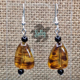 May include: A pair of dangle earrings with amber-colored glass beads and black beads. The beads are teardrop shaped and have a marbled pattern.