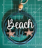 May include: Wooden beach-themed ornament with the words "Beach Life" in white script. The ornament features two starfish and a blue and brown color scheme. A wooden bead and twine are attached for hanging.