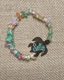 May include: A multi-colored gemstone bracelet with a variety of colors including green, pink, yellow, and orange. The bracelet is made of small, irregular shaped stones. The bracelet is on a brown burlap background with a logo for Salty Creations.