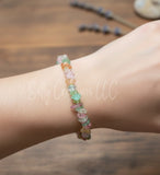 Handmade rainbow fluorite crystal chip bracelet worn on a wrist over a rustic wooden background