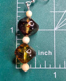 Square-shaped earring with a grainy, golden brown pattern on a measuring mat..