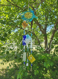 Handmade turquoise turtle wind chime hanging from a tree with blue beads, charms, and decorative glass pieces in a sunny garden setting