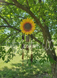 Handcrafted sunflower wind chime with rustic metal plates hanging from a tree in a sunny backyard.