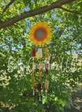 Handmade yellow sunflower glass wind chime with colorful glass pendants hanging from a tree branch.
