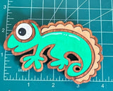 Colorful handcrafted wooden chameleon fridge magnets displayed in a grid on a measuring mat.