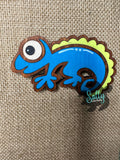 Blue and yellow handcrafted wooden chameleon fridge magnets displayed in a grid on a textured background
