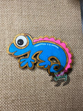 Blue and Pink handcrafted wooden chameleon fridge magnets displayed in a grid on a textured background