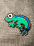 Green and blue handcrafted wooden chameleon fridge magnets displayed in a grid on a textured background