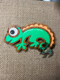Green and orange handcrafted wooden chameleon fridge magnets displayed in a grid on a textured background