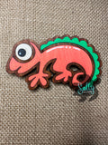 Orange and green handcrafted wooden chameleon fridge magnets displayed in a grid on a textured background