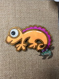 Orange and purple handcrafted wooden chameleon fridge magnets displayed in a grid on a textured background