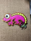 Purple and yellow handcrafted wooden chameleon fridge magnets displayed in a grid on a textured background