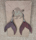  A pair of wooden earrings shaped like a mermaid tail. The earrings are a dark reddish brown color and have silver hooks.