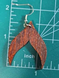 A pair of wooden earrings shaped like a whale tail. The earrings are a dark reddish brown color and have a silver hook.